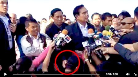 Thailand Prime Minister Prayut Chan-ocha scratches the ear of a Thai journalist squatting before him while conducting a media briefing.
