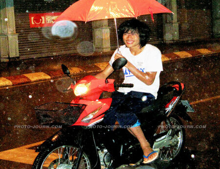 A motorcyclist tries to shelter himself from heavy rain while riding a motorcycle in Thailand