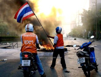 A red-shirt protester waves a Thai flag in defiance at government troops on the other side of a "life fire zone" in Rama IV, Bon Kai
